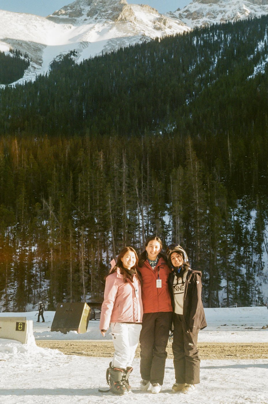 Three friends bundled up in front of a forested mountainside