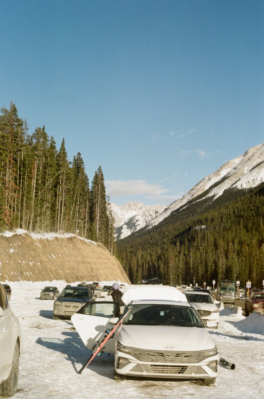 Cars parked in a snowy lot with mountains behind