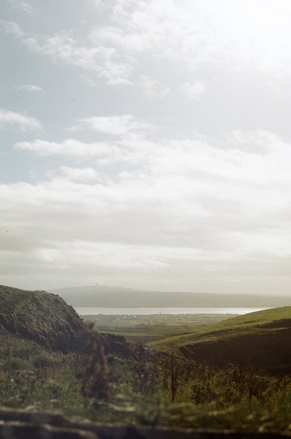 Green hills leading down to the sea under a cloudy sky