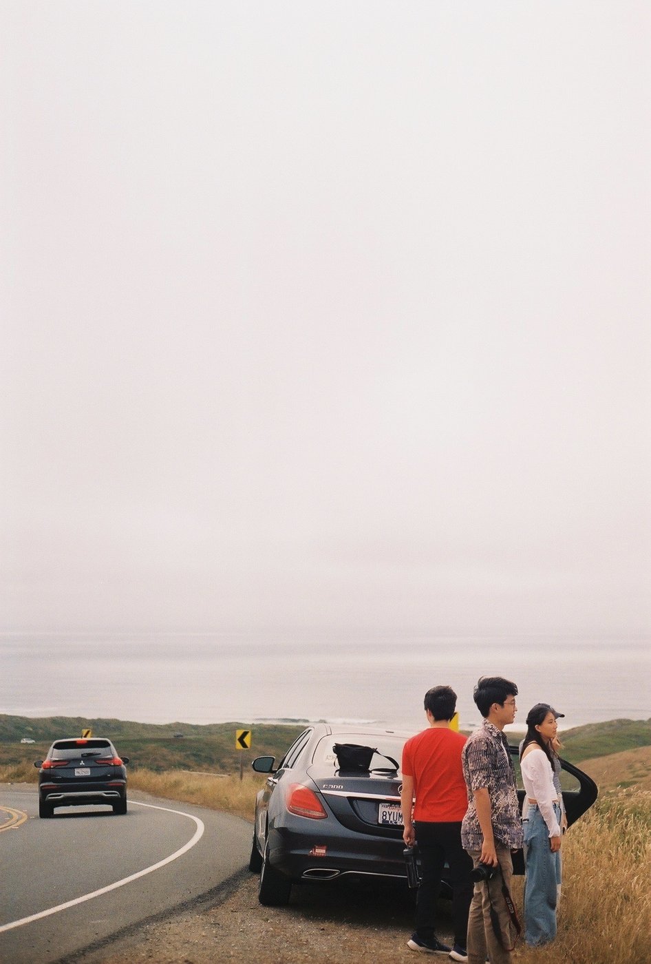 Friends standing by a car on a coastal road