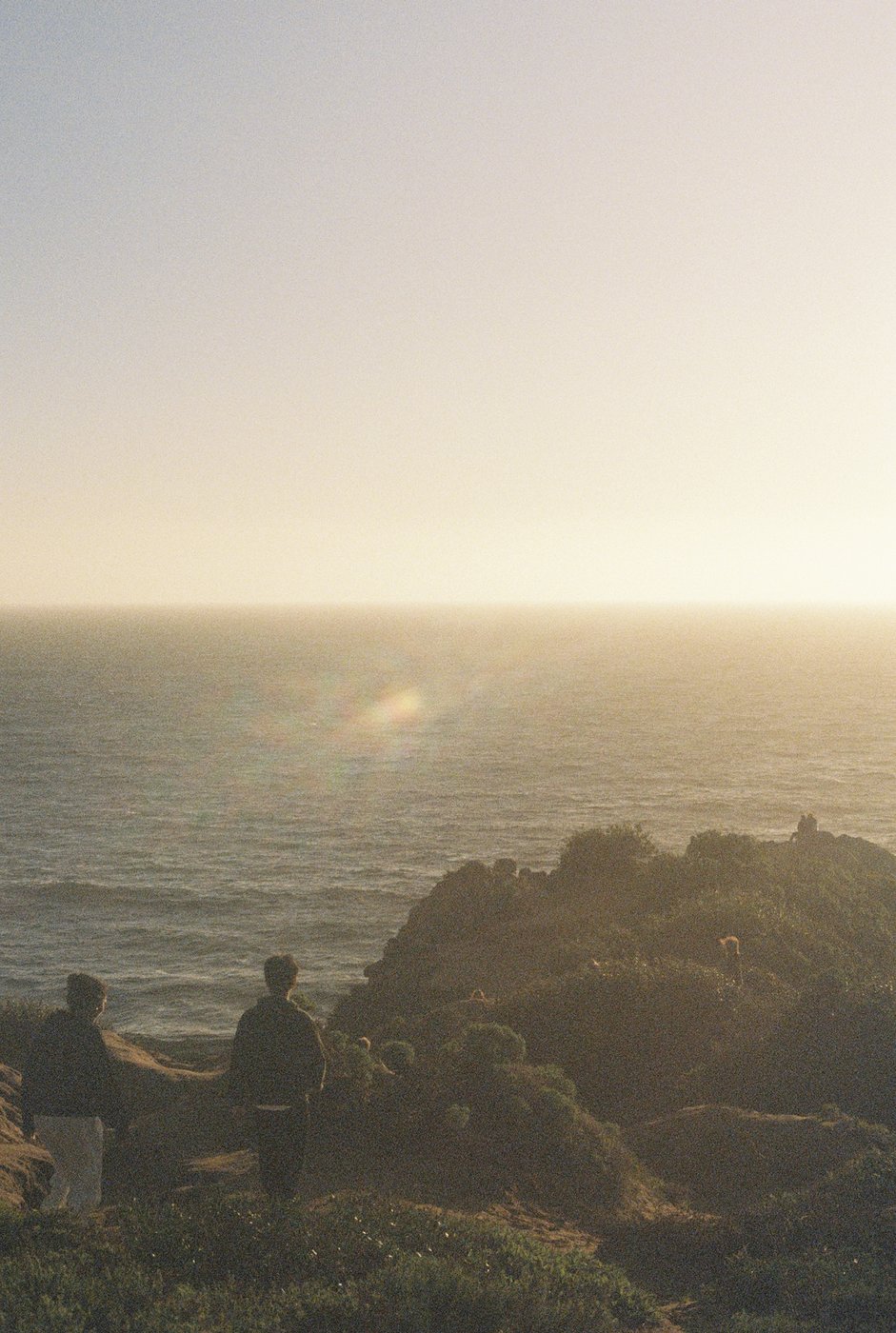 Two people sitting on rocks watching the sunset over the ocean