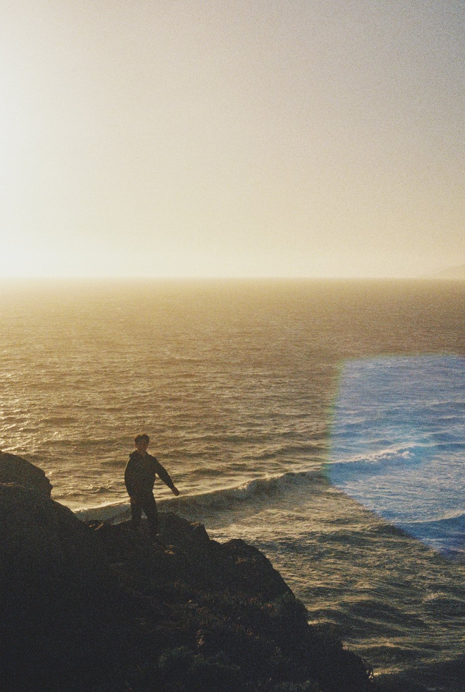 A person standing on rocks watching the waves at sunset