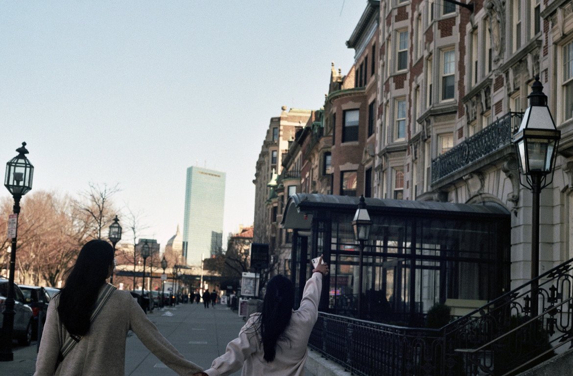 Two friends walking arm in arm down a Boston street